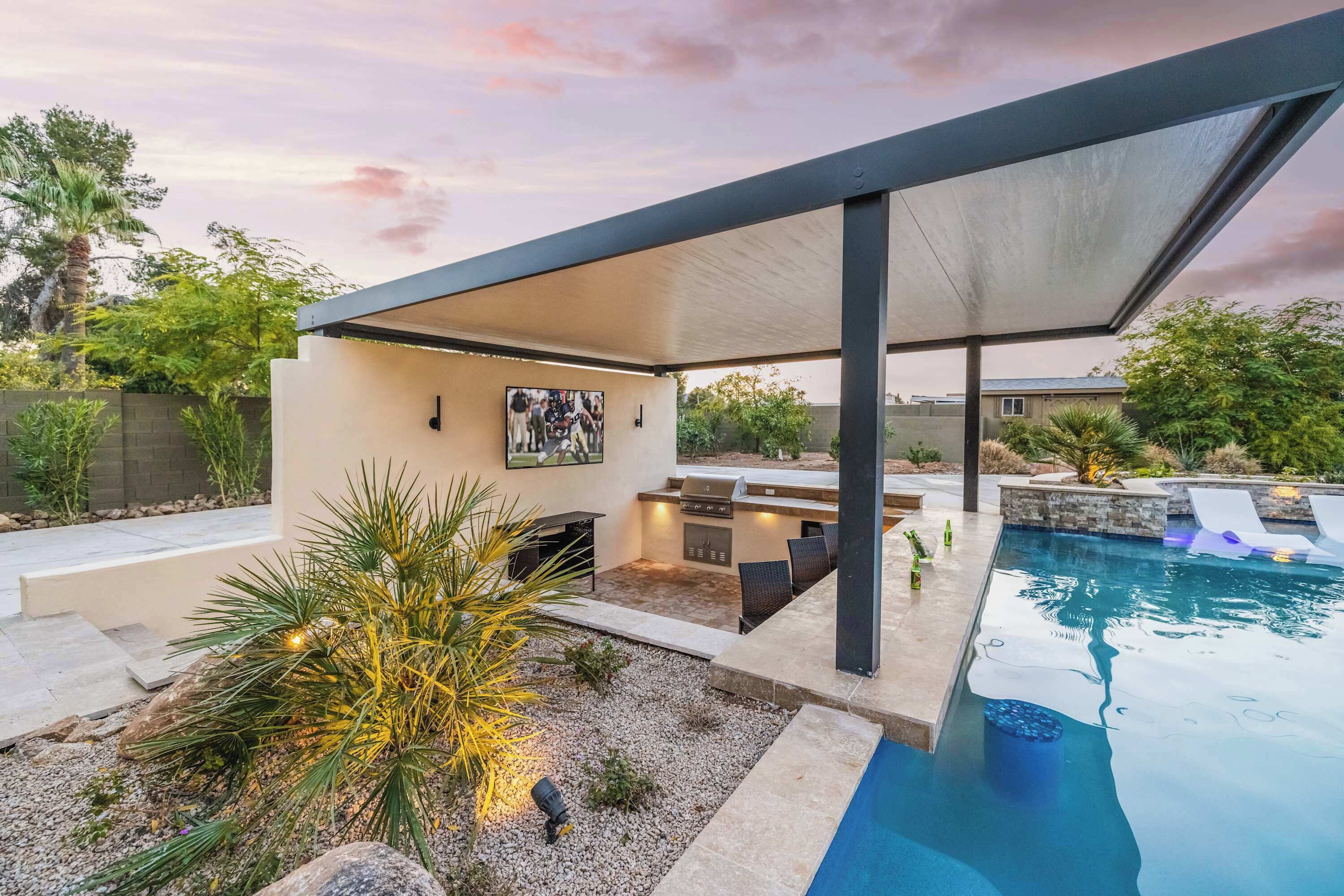 A modern outdoor patio with a pool, seating area, and grilling station.