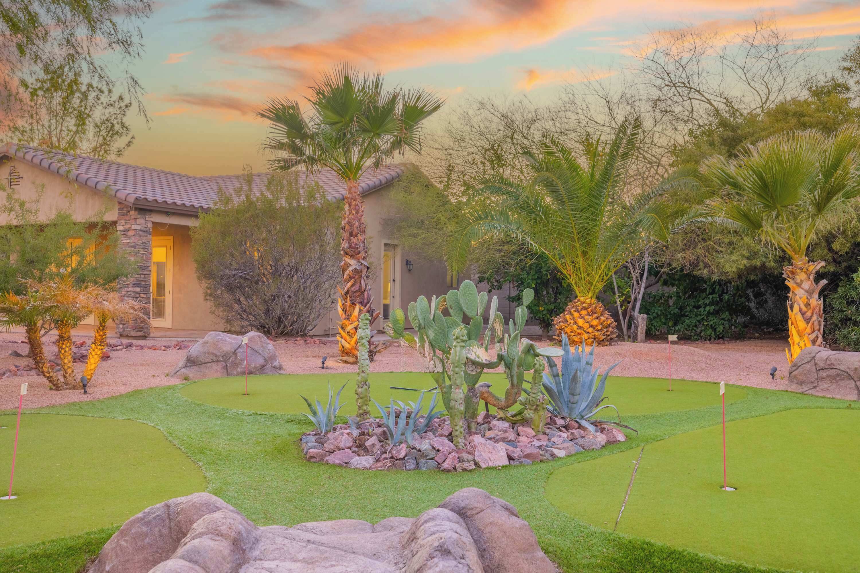 Un campo de golf con una casa al fondo, rodeado de cactus y palmeras.