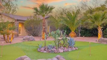 Un campo de golf con una casa al fondo, rodeado de cactus y palmeras.