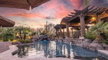 A pool area with a waterfall feature, stone architecture, and a pergola structure.