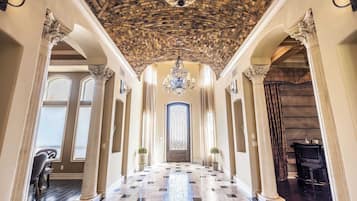 A grand hallway with a vaulted ceiling, a chandelier, and a large door with a stained glass window.