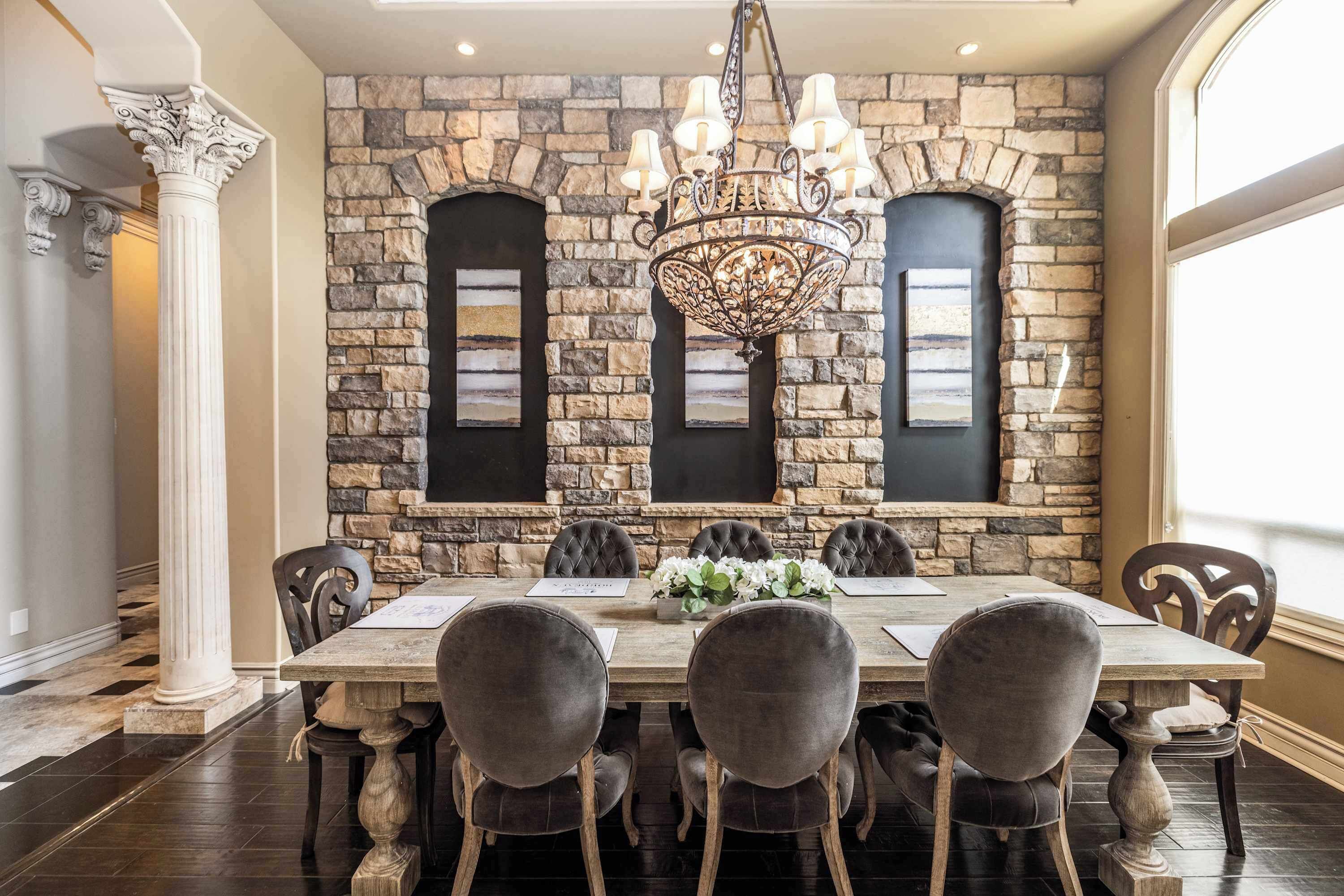 A dining room with a stone wall, a chandelier, and a large table with chairs.
