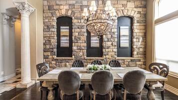 A dining room with a stone wall, a chandelier, and a large table with chairs.