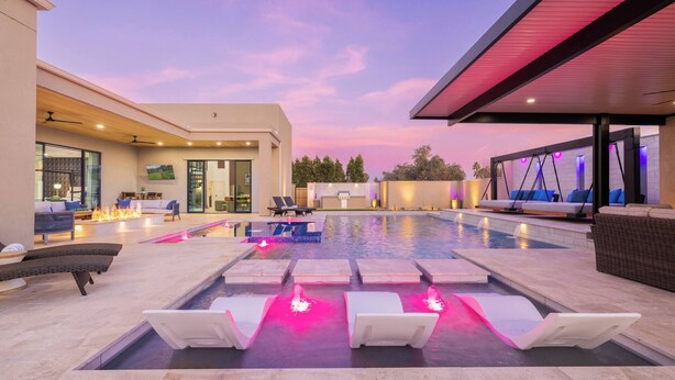 A modern outdoor pool area with lounge chairs, a fire feature, and a covered seating area. - HÓZHÓ | Pool, Hot Tub, Theatre, Sauna & Fire Pit (Scottsdale)