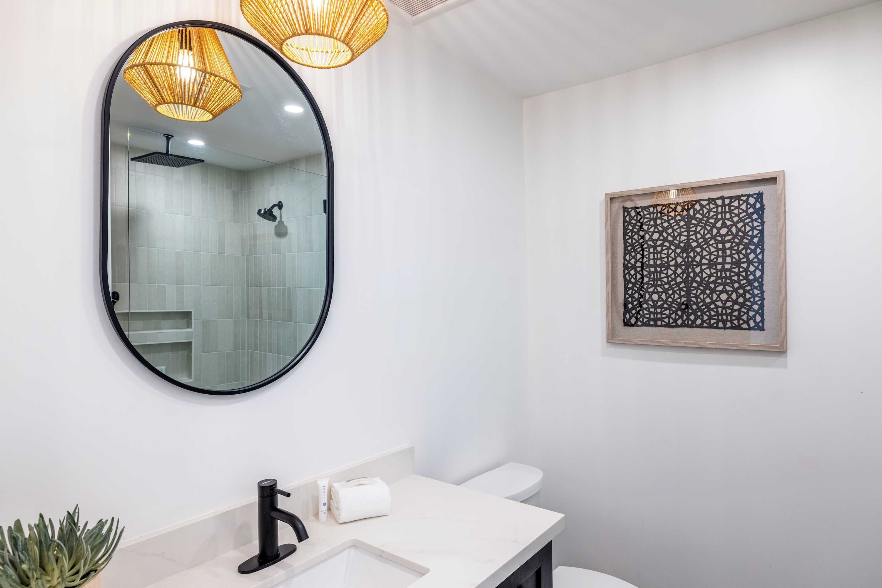 A modern bathroom with a round mirror, a black faucet, a white sink, a toilet, and a decorative wall piece.