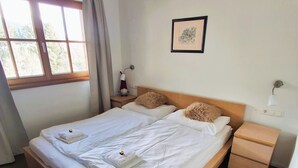 A neatly made double bed with white linens, a wooden headboard, a bedside table with a lamp, and a window with curtains. - Ski-in/Ski-out directly next to the gondola – KitzSki (Mittersill)