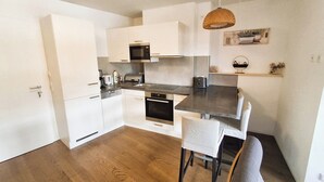 A compact kitchen with white cabinets, a microwave, a toaster, and a wooden dining table with a chair. - Ski-in/Ski-out directly next to the gondola – KitzSki (Mittersill)