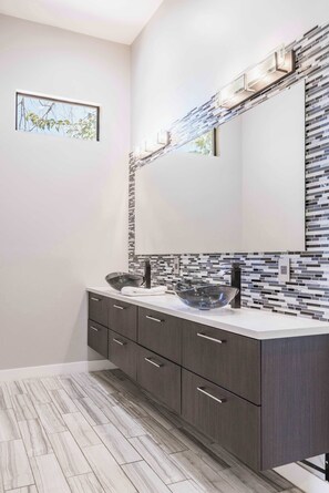 A modern bathroom with a large mirror, dark cabinetry, and a tiled backsplash. - HÓZHÓ | Pool, Hot Tub, Putting Green & Game Room (Scottsdale)