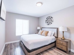 A bedroom with a bed, bedside tables, a wall clock, and a window. - HÓZHÓ | Pool, Hot Tub, Putting Green & Game Room (Scottsdale)