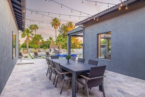 An outdoor patio with a table and chairs, a pergola, and string lights. - HÓZHÓ | Pool, Hot Tub, Putting Green & Game Room (Scottsdale)