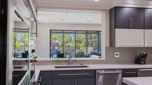 Une cuisine moderne dotée d’une grande fenêtre, d’appareils électroménagers en acier inoxydable et de meubles de rangement aux couleurs sombres.