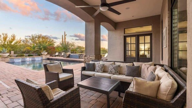 Une terrasse extérieure avec une piscine, des meubles en osier et un ventilateur de plafond.