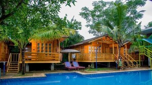 A wooden cabin with a pool, surrounded by lush greenery.