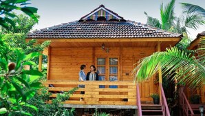 A wooden cabin with a balcony, surrounded by lush greenery.