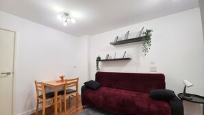 Ett rum med ett matbord i trä, en röd soffa, ett litet sidobord och en vägghylla med växter.