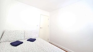 Ett sovrum med en säng, två kuddar, en dörr och en lampa.