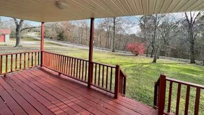 A covered porch with a red railing, a view of a grassy yard, and trees in the background.