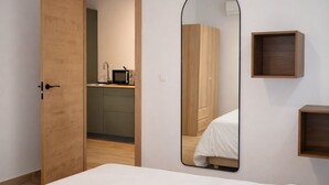 Ein Schlafzimmer mit Holztür, einem Bett, einem Spiegel, einer kleinen Holzkabine und einer Küchenzeile im Hintergrund.