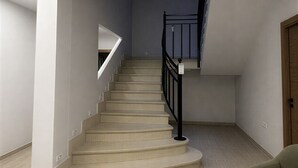 Un escalier avec une rampe, un plancher de couleur claire et un canapé vert dans une pièce aux murs blancs.