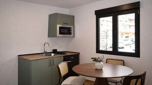 A compact kitchen with a microwave, sink, and cabinets, a round dining table with chairs, and a window with a view of buildings. - Collection Las Ventas Apartment 1D near the Bullring (Madrid)