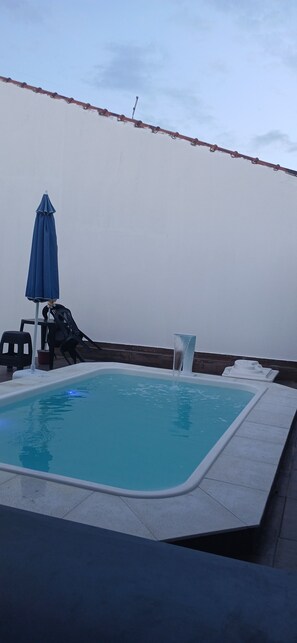 A swimming pool with a blue umbrella, a chair, and a small table. - House on the beach in Peruíbe (Peruíbe)
