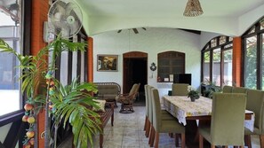 A dining area with a table set for four, surrounded by chairs, a fan, and potted plants.