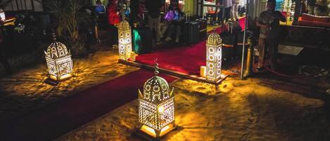 Una zona arenosa con faroles ornamentados e iluminados y una alfombra roja.