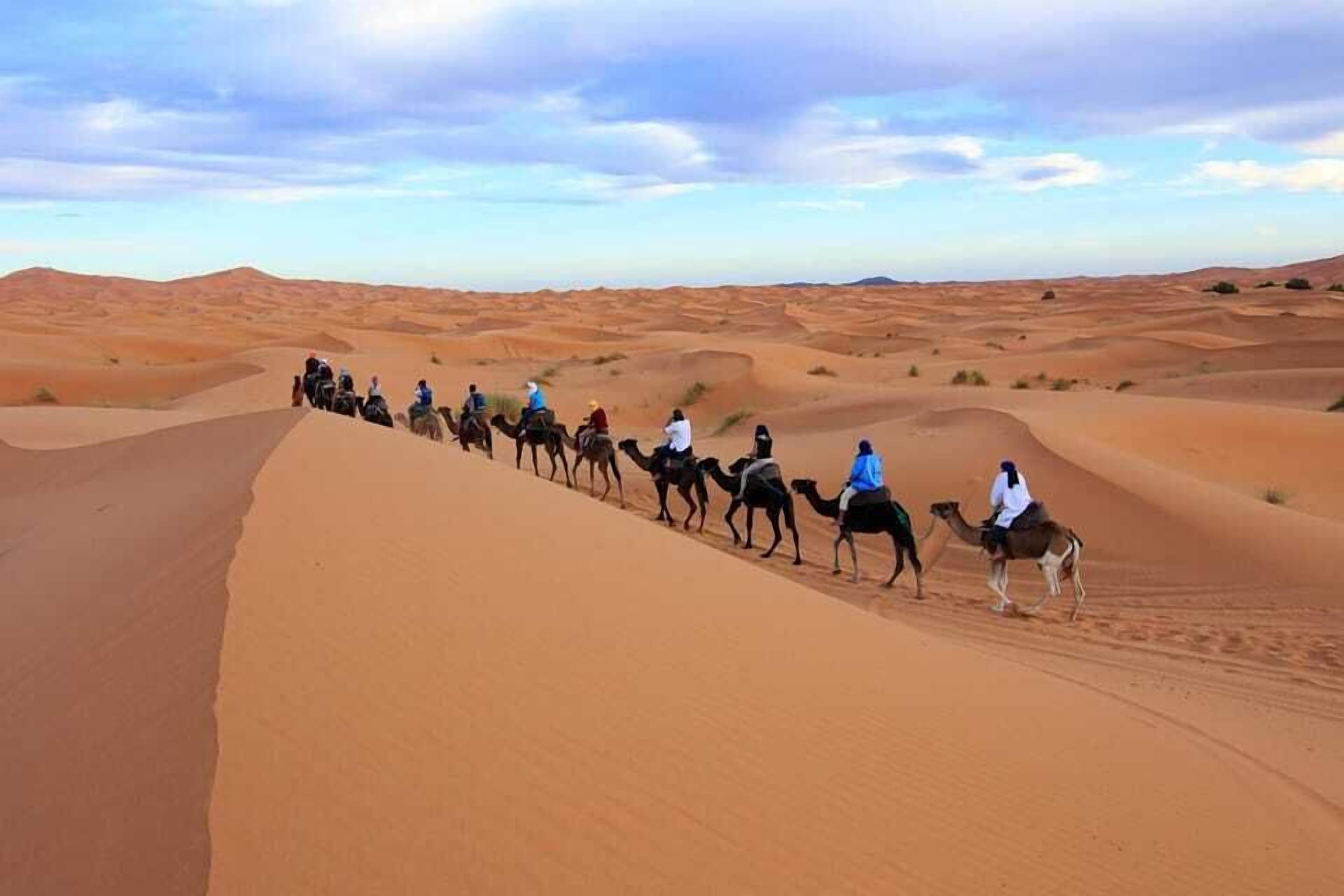 A group of people riding camels through a desert landscape with sand dunes.