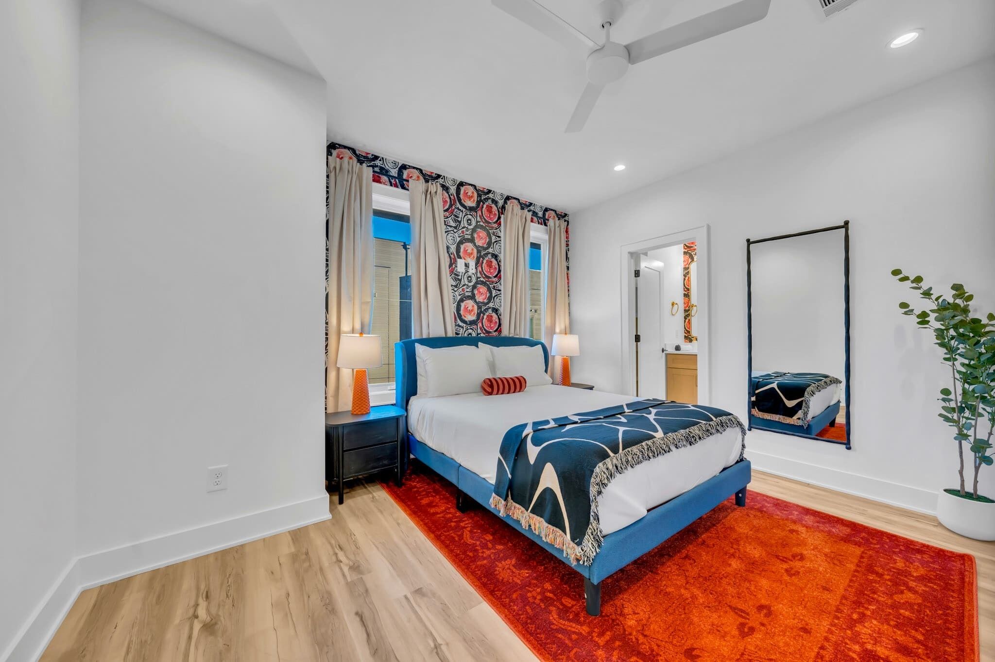 A modern bedroom with a bed, nightstands, a mirror, and a red carpet.