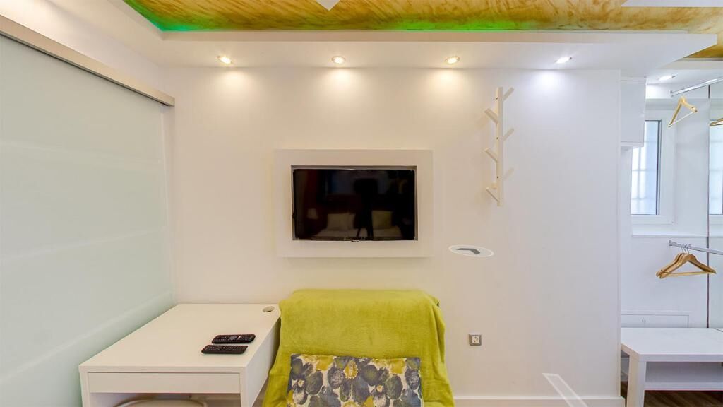 Een moderne kamer met een bed, een aan de muur bevestigde televisie, een klein tafeltje en een hanglamp.