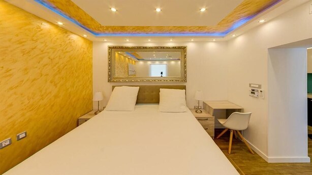 Une chambre d’hôtel dotée d’un grand lit, de tables de chevet, d’un bureau, d’une chaise, d’un miroir et d’un plafond équipé de luminaires encastrés.