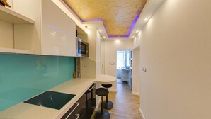 Une cuisine moderne dotée d’une cuisinière intégrée, un coin repas avec des tabourets et un couloir menant à une salle de bain.