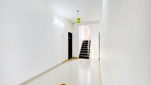 A hallway with a staircase leading to an upper floor, white walls, and a patterned floor design. - Deluxe Guna Residency (Tirupporur)