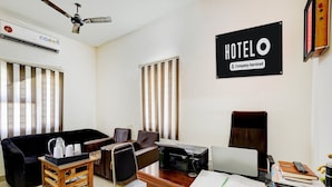 A hotel room with a desk, chairs, a sofa, an air conditioner, a ceiling fan, and a sign indicating it is a company-serviced hotel. - Deluxe Guna Residency (Tirupporur)