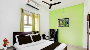 A bedroom with a bed, a nightstand, an air conditioner, a ceiling fan, and a green wall. - Deluxe Guna Residency (Tirupporur)