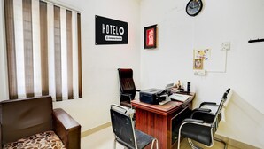 A hotel room with a desk, two chairs, a sofa, a clock, and a sign indicating the room is company serviced. - Deluxe Guna Residency (Tirupporur)