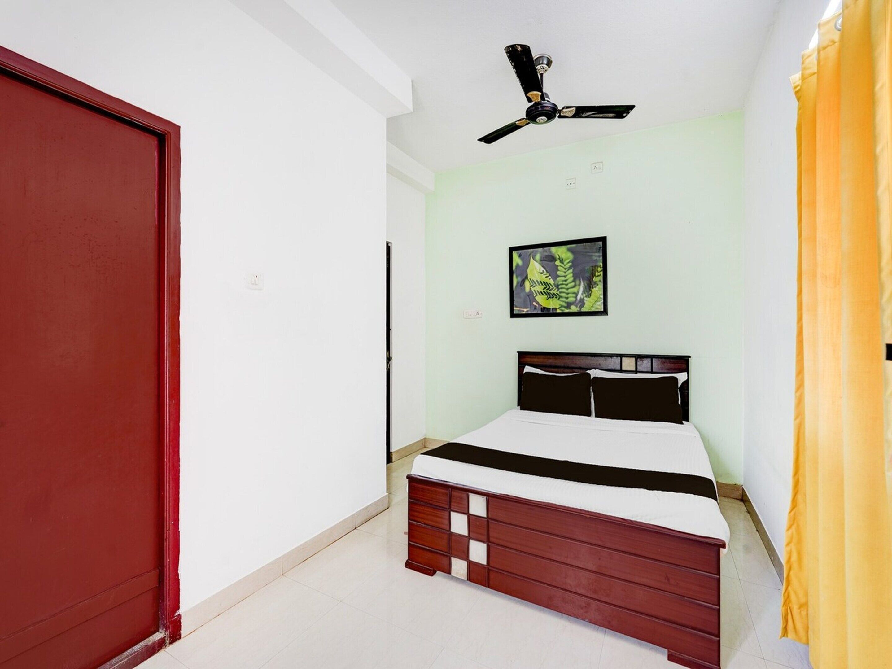 A bedroom with a bed, a ceiling fan, a door, and a framed picture on the wall.