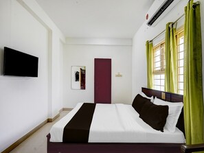 Ein Hotelzimmer mit Bett, Flachbildfernseher, Tür und einem Fenster mit Vorhängen.