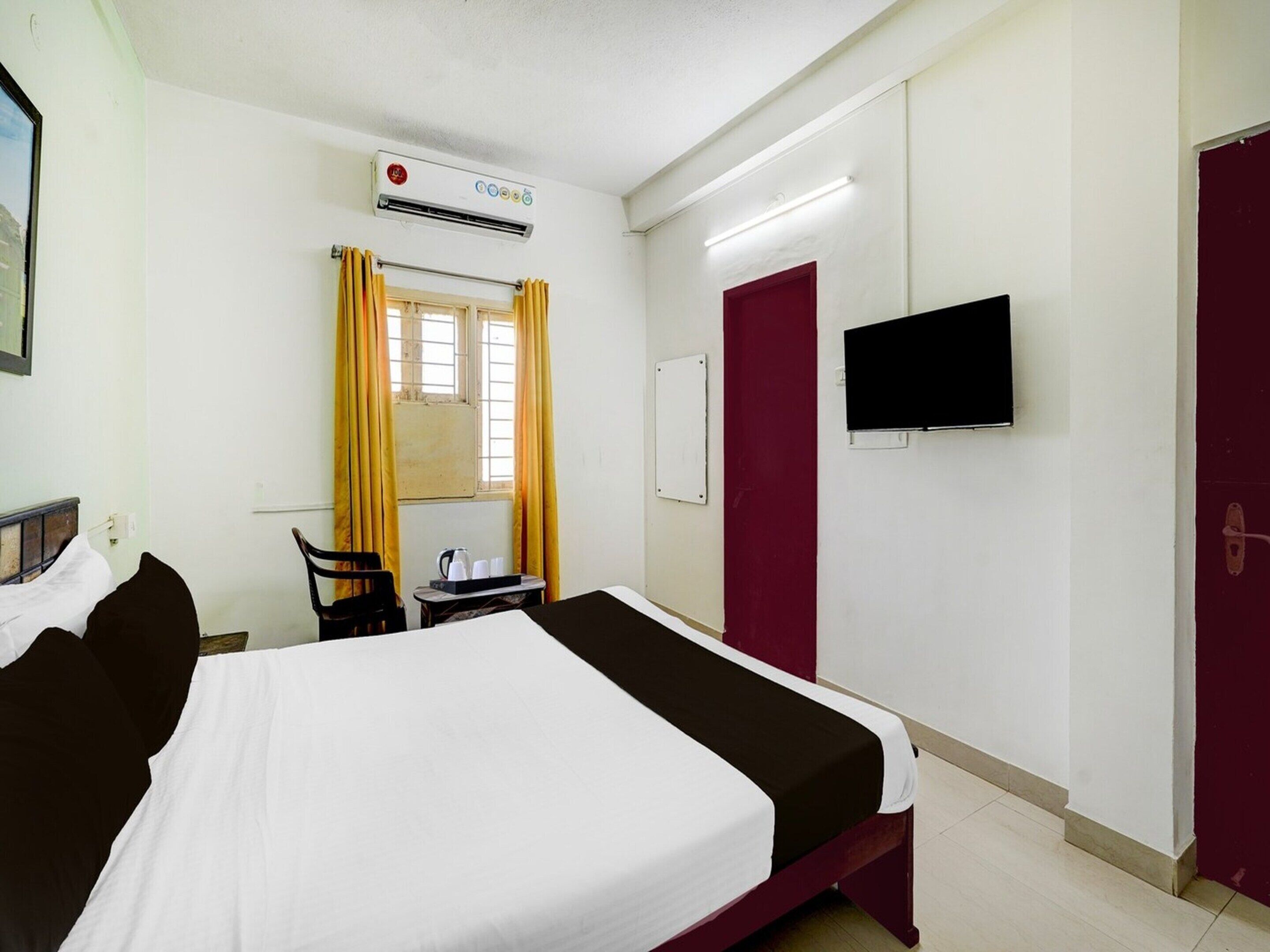 Une chambre d’hôtel comprenant un lit, un bureau avec une chaise, un appareil de climatisation, un téléviseur et une porte.