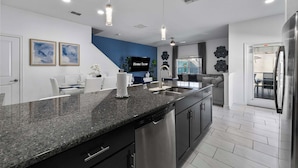 Una cucina moderna con piani di lavoro in granito, elettrodomestici in acciaio inossidabile, illuminazione a sospensione e una parete d'accento blu.