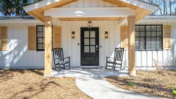 A house with a porch, two rocking chairs, a black door, and wooden siding.