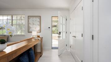 A hallway with a wooden bench, a white door, and a window with blinds.