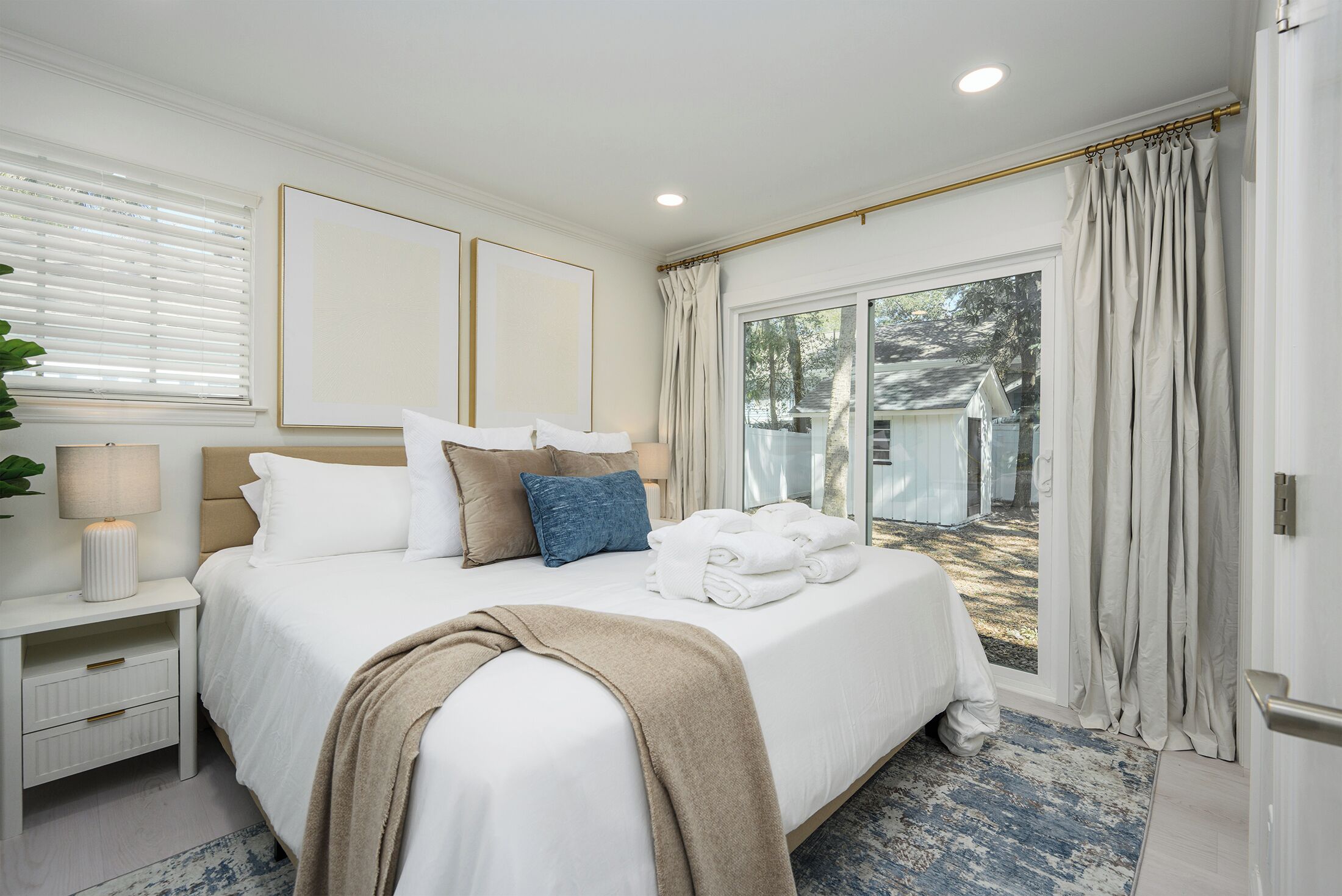 A bedroom with a large bed, a nightstand, a lamp, and a view of the outside.