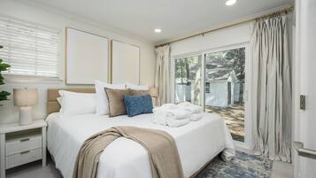 A bedroom with a large bed, a nightstand, a lamp, and a view of the outside.