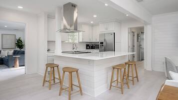 A modern kitchen with white cabinetry, a central island with stools, stainless steel appliances, and a large window.