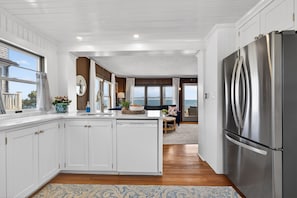 A kitchen with white cabinetry, a stainless steel refrigerator, and a view of the ocean. - Oceanfront with Views! Sleeps 10, Central AC! (Scituate)