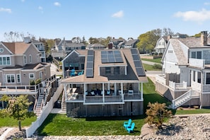 A residential property with a covered deck, solar panels, and a stone facade. - Oceanfront with Views! Sleeps 10, Central AC! (Scituate)