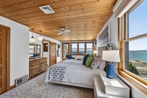 A bedroom with a bed, a dresser, a nightstand, a lamp, and a view of the sea. - Oceanfront with Views! Sleeps 10, Central AC! (Scituate)