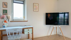 Una stanza con una scrivania, una sedia, una TV su un mobile e una finestra.