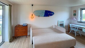 Una camera da letto con un letto, una scrivania, una sedia, una cassettiera e un’asse da surf appesa al muro.